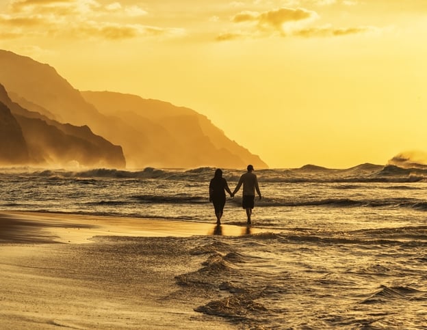 Silhouette of a couple at sunset walking along a Hawaiian beach.