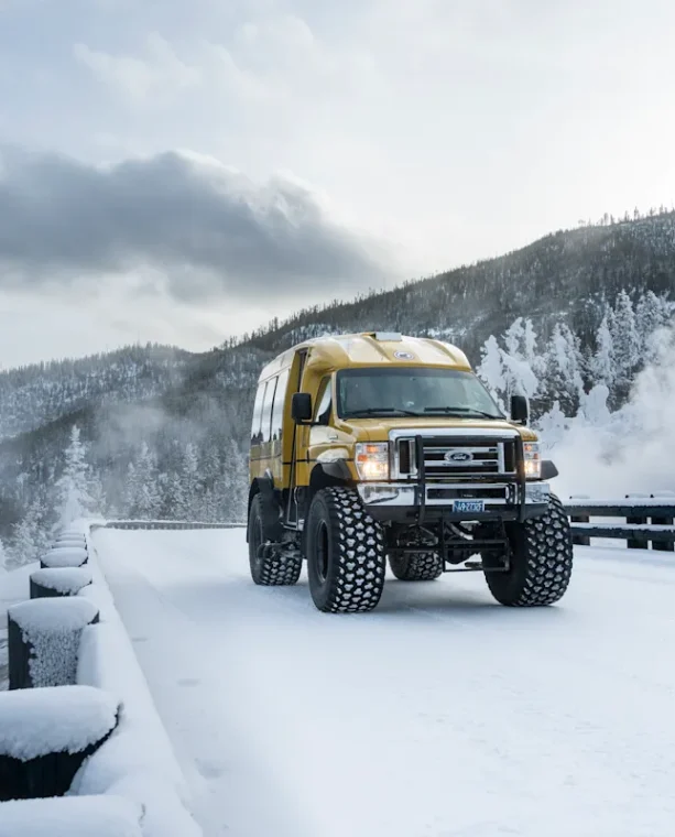 Snowcoach crossing snow-covered bridge with fumarole